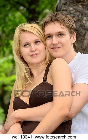 Loving white engaged couple with man embracing woman in a park View Large Photo Image Stock Image - Loving white engaged couple with man embracing woman in a park. Fotosearch