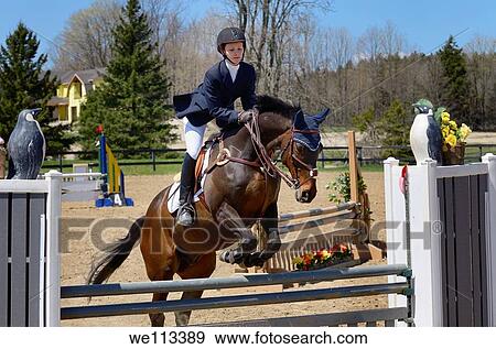 Teenage girl taking off on her horse over a jump at an outdoor equestrian show competition View Large Photo Image Stock Photo - Teenage girl taking off on her horse over a jump at an outdoor equestrian show competition. Fotosearch