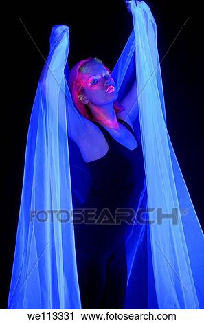 Stock Image - Woman in a dark room with fluorescent paint makeup holding a white veil under black lights. Fotosearch