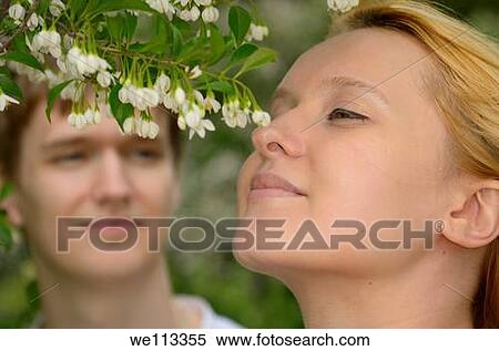 Blond woman smelling flowers in a park while her fiance watches View Large Photo Image Stock Photography - Blond woman smelling flowers in a park while her fiance watches. Fotosearch
