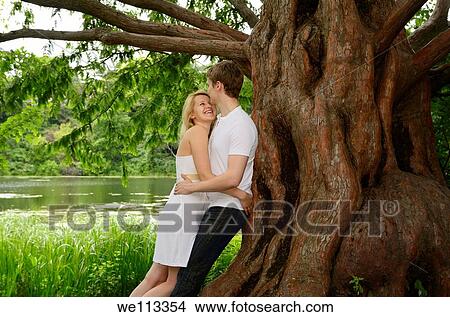 Happy couple embracing under a large Dawn Redwood tree on the shore of a lake View Large Photo Image Picture - Happy couple embracing under a large Dawn Redwood tree on the shore of a lake. Fotosearch