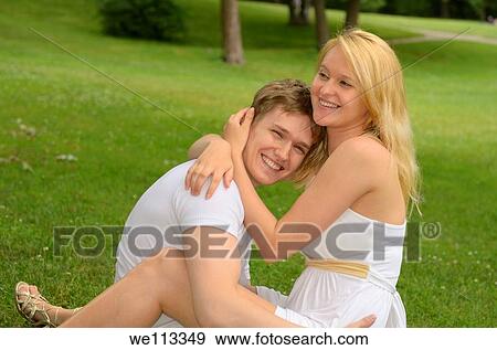 Happy smiling white couple embracing while lounging on a field of grass in a park View Large Photo Image Stock Photo - Happy smiling white couple embracing while lounging on a field of grass in a park. Fotosearch