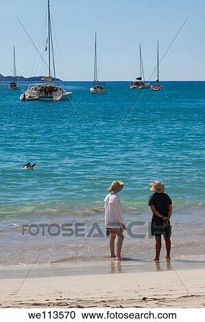 Man and woman in matching hats wading in the water on the beach with sailboats moored off shore View Large Photo Image Stock Image - Man and woman in matching hats wading in the water on the beach with sailboats moored off shore. Fotosearch