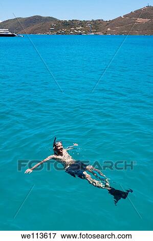 Man in snorkel gear smiling and relaxing in turquoise water in front of town of Leverick Bay in British Virgin Islands View Large Photo Image Stock Photo - Man in snorkel gear smiling and relaxing in turquoise water in front of town of Leverick Bay in British Virgin Islands. Fotosearch