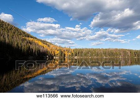 Stock Photograph - Orange and yellow aspen trees on hillside reflecting in water of Bear Lake in Rocky Mountain National Park in Colorado. Fotosearch