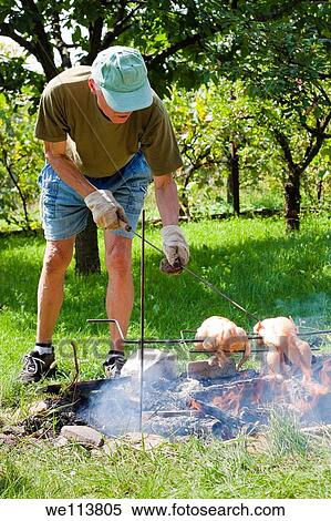 Stock Photography - Senior man grilling chickens on bonfire. Fotosearch