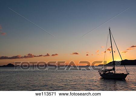 Silhouette of sailboat moored in water with orange glow of sunset lighting up the clouds and sky in Caribbean View Large Photo Image Stock Image - Silhouette of sailboat moored in water with orange glow of sunset lighting up the clouds and sky in Caribbean. Fotosearch