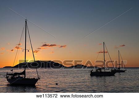 Silhouette of sailboats moored in water with orange glow of sunset lighting up the clouds and sky in Caribbean View Large Photo Image Stock Image - Silhouette of sailboats moored in water with orange glow of sunset lighting up the clouds and sky in Caribbean. Fotosearch