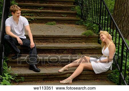 Stock Image - Smiling couple looking at each other while sitting on stone stairs in a park. Fotosearch