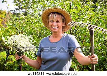 Portrait of happy mature woman holding flowers and rake in the garden View Large Photo Image Stock Image - Portrait of happy mature woman holding flowers and rake in the garden. Fotosearch