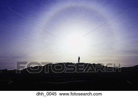 Stock Photography - A silhouette of a person standing on top of a mountain. Fotosearch