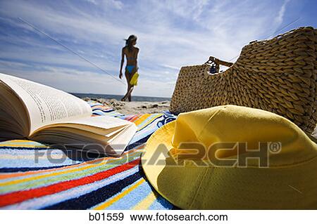 Beach towel with book and bag with a young woman in background View Large Photo Image Stock Photo - Beach towel with book and bag with a young woman in background. Fotosearch