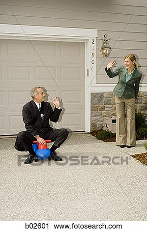 Stock Image - Businessman riding on a toy waving at a businesswoman. Fotosearch