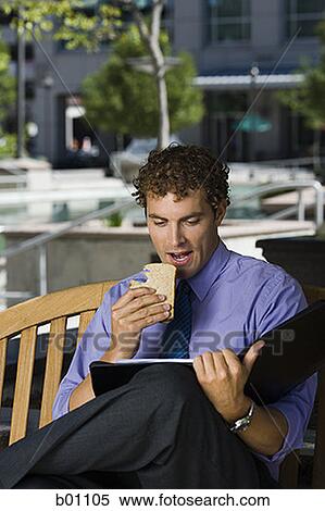 Businessman sitting on a bench, eating a sandwich View Large Photo Image Stock Photography - Businessman sitting on a bench, eating a sandwich. Fotosearch