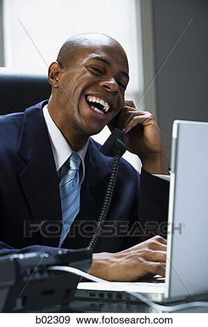 Businessman working on a laptop computer and talking on the phone View Large Photo Image Stock Photo - Businessman working on a laptop computer and talking on the phone. Fotosearch
