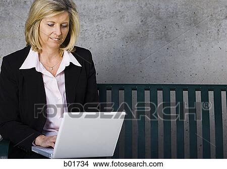 Businesswoman sitting on a bench and using a laptop View Large Photo Image Picture - Businesswoman sitting on a bench and using a laptop. Fotosearch