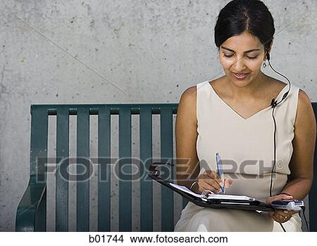 Businesswoman sitting on a bench and writing in a diary View Large Photo Image Picture - Businesswoman sitting on a bench and writing in a diary. Fotosearch
