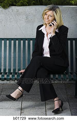 Businesswoman sitting on a bench and talking on a mobile phone View Large Photo Image Stock Photo - Businesswoman sitting on a bench and talking on a mobile phone. Fotosearch