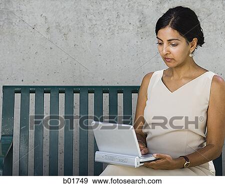 Businesswoman sitting on a bench and using a laptop View Large Photo Image Stock Photo - Businesswoman sitting on a bench and using a laptop. Fotosearch