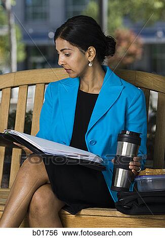 Businesswoman sitting on a bench and reading documents in a coffee break View Large Photo Image Stock Photograph - Businesswoman sitting on a bench and reading documents in a coffee break. Fotosearch