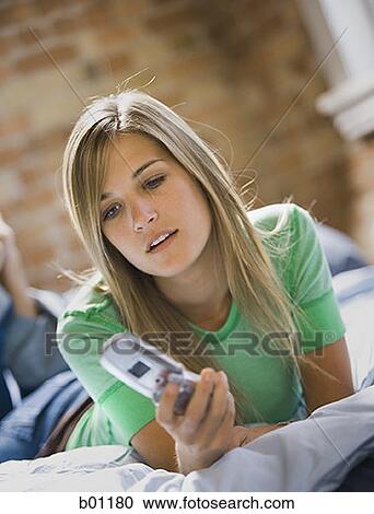 Close-up of a teenage girl holding a mobile phone lying on the bed View Large Photo Image Stock Image - Close-up of a teenage girl holding a mobile phone lying on the bed. Fotosearch