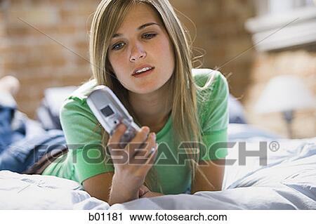 Close-up of a teenage girl holding a mobile phone lying on the bed View Large Photo Image Stock Image - Close-up of a teenage girl holding a mobile phone lying on the bed. Fotosearch