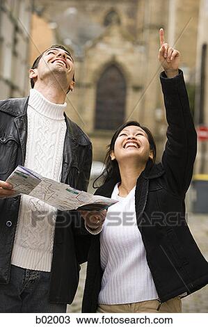 Stock Image - Close-up of a young couple holding a map and looking up. Fotosearch