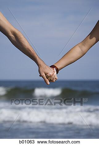 Stock Image - Close-up of a young couple holding hands. Fotosearch