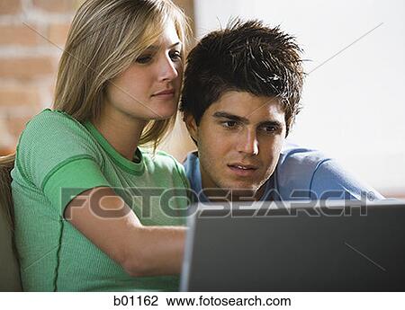 Close-up of a young couple looking at a laptop View Large Photo Image Stock Image - Close-up of a young couple looking at a laptop. Fotosearch