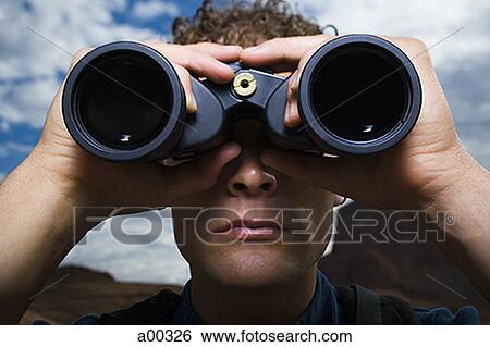 Close-up of a young man looking through binoculars View Large Photo Image Stock Photograph - Close-up of a young man looking through binoculars. Fotosearch