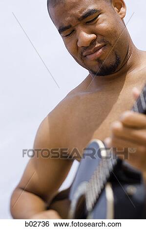 Close-up of a young man playing a guitar View Large Photo Image Stock Photograph - Close-up of a young man playing a guitar. Fotosearch