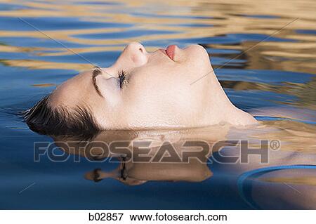 Close-up of a young woman floating on the surface of a lake View Large Photo Image Stock Photo - Close-up of a young woman floating on the surface of a lake. Fotosearch