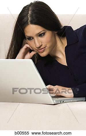 Close-up of a young woman lying on a couch and using a laptop View Large Photo Image Stock Photography - Close-up of a young woman lying on a couch and using a laptop. Fotosearch