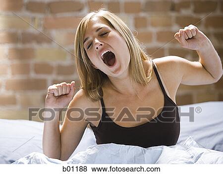 Close-up of a young woman sitting on a bed yawning View Large Photo Image Stock Photo - Close-up of a young woman sitting on a bed yawning. Fotosearch