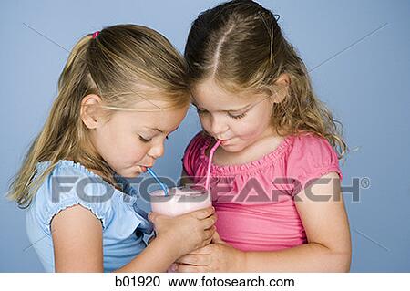 Stock Image - Close-up of two sisters sharing a milkshake. Fotosearch