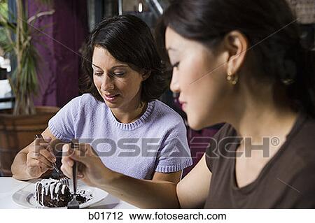 Stock Image - Close-up of two women sharing a dessert in a cafe. Fotosearch