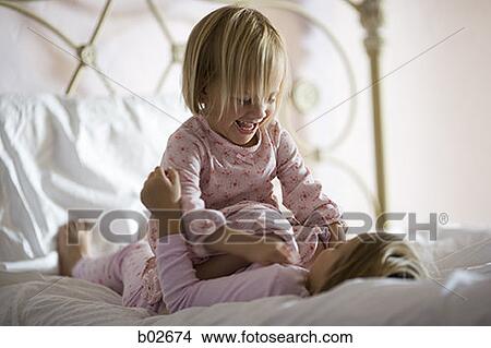 Girl sitting on top of her sister on the bed View Large Photo Image Picture - Girl sitting on top of her sister on the bed. Fotosearch