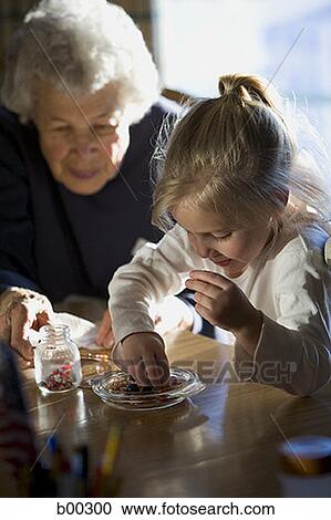Stock Image - Grandmother sitting with her granddaughter at a dining table. Fotosearch