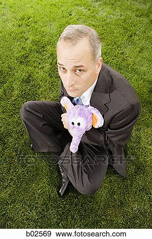 High angle view of a businessman with hugging a toy sitting on a lawn View Large Photo Image Stock Photo - High angle view of a businessman with hugging a toy sitting on a lawn. Fotosearch