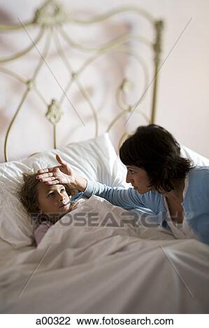 Stock Image - High angle view of a mother checking her daughter's temperature. Fotosearch