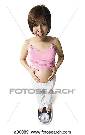 Stock Photo - High angle view of a pregnant woman standing on a bathroom scale. Fotosearch