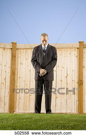 Stock Photo - Low angle view of a businessman standing in front of a wall looking down. Fotosearch