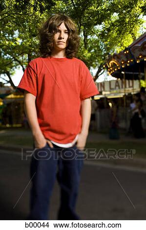 Picture - Low angle view of a long-haired teenage boy standing with hands in his pockets. Fotosearch