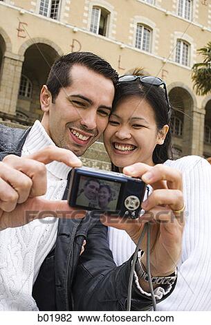 Low angle view of a young couple taking a photograph of themselves View Large Photo Image Stock Image - Low angle view of a young couple taking a photograph of themselves. Fotosearch
