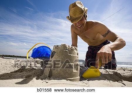 Stock Photo - Low angle view of a young man digging sand on the beach. Fotosearch