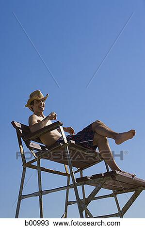 Low angle view of a young man sitting on a lifeguard chair View Large Photo Image Stock Image - Low angle view of a young man sitting on a lifeguard chair. Fotosearch