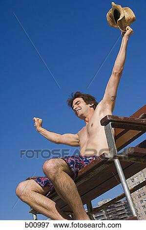 Low angle view of a young man sitting on a lifeguard chair View Large Photo Image Stock Photo - Low angle view of a young man sitting on a lifeguard chair. Fotosearch