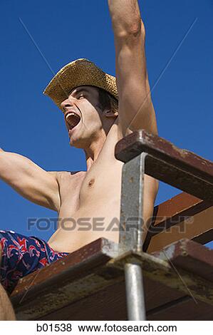 Stock Photo - Low angle view of a young man sitting in lifeguard chair and shouting. Fotosearch
