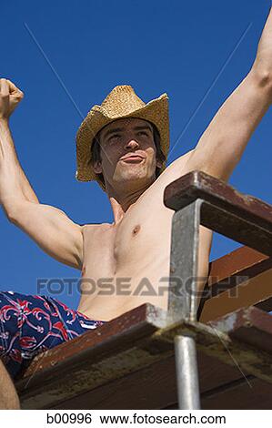 Low angle view of a young man sitting on a lifeguard chair View Large Photo Image Stock Photograph - Low angle view of a young man sitting on a lifeguard chair. Fotosearch