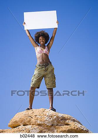Low angle view of a young woman holding a blank sign View Large Photo Image Stock Photo - Low angle view of a young woman holding a blank sign. Fotosearch